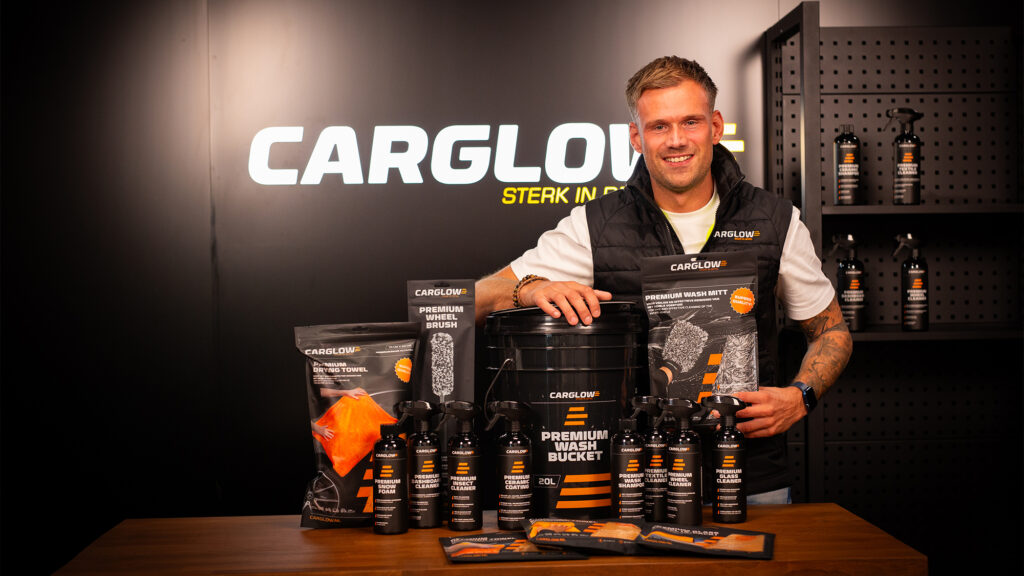 Medewerker van CARGLOW voor een zwarte auto met een microvezeldoek en autoverzorgingsproduct in zijn handen.