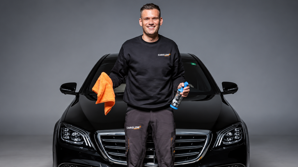Medewerker van CARGLOW voor een zwarte auto met een microvezeldoek en autoverzorgingsproduct in zijn handen.
